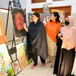 Visitors look at paintings by street children at an exhibition held on International Day of Artists at Peshawar University on Oct 22, 2025.