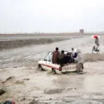 A vehicle carrying people is trying to cross a flooded stream in KP, July 2026.